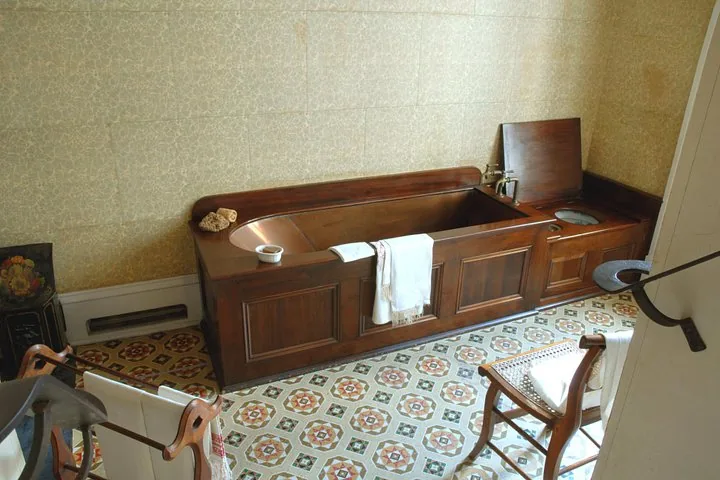 Antike Holzbadewanne und Badezimmerarmaturen auf einem Fliesenboden